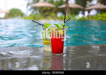 Classica e fragola cocktail mojito al bordo di una piscina del resort. Concetto di vacanza di lusso. Piscina all'aperto sullo sfondo Foto Stock