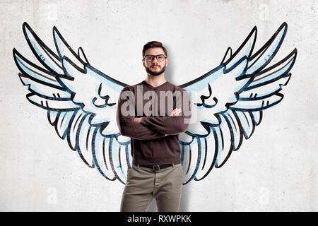 Uomo con occhiali di indossare un abbigliamento informale con le ali disegnate sulla parete sullo sfondo Foto Stock