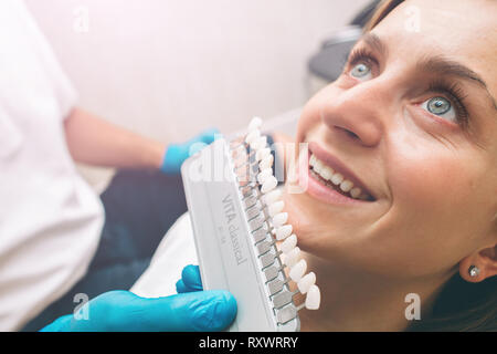 Ritratto di un dentista che considera i denti della giovane donna paziente. Il controllo e la selezione di colore della giovane donna di denti Foto Stock