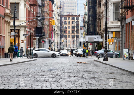 NEW YORK CITY - circa 2019: coperto in ciottoli di Greene Street nel quartiere di SoHo è occupato con auto e persone in Manhattan NYC. Foto Stock