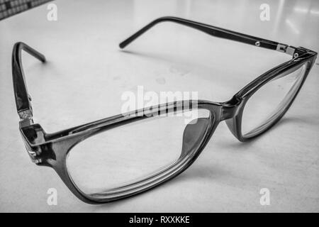 Foto in bianco e nero di occhiali mantenuta su un tavolo bianco Foto Stock