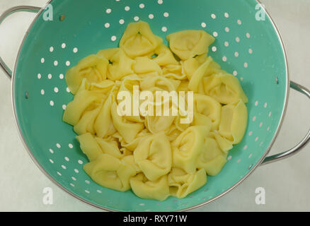 Close up di bollito formaggio tortelloni di svuotamento nel colapasta blu su sfondo bianco Foto Stock