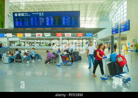 FRANKFURT AM MAIN, Germania - 29 agosto 2018: Frankfurt international airport terminal, donna con carrello portabagagli, i passeggeri in attesa su sedie sotto ti Foto Stock