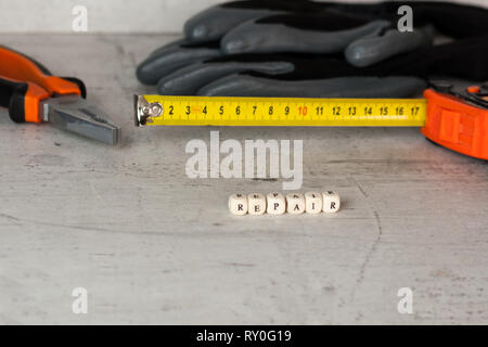 Costruzione nero guanti e un metro a nastro sullo sfondo di un muro di cemento. In primo piano l'iscrizione riparazione. Foto Stock