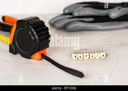 Costruzione nero guanti e un metro a nastro sullo sfondo di un muro di cemento. In primo piano l'iscrizione riparazione. Foto Stock