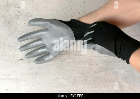 Un uomo mette su un guanto sulla mano per le riparazioni. Mano sul calcestruzzo leggero sottofondo. Vista frontale Foto Stock