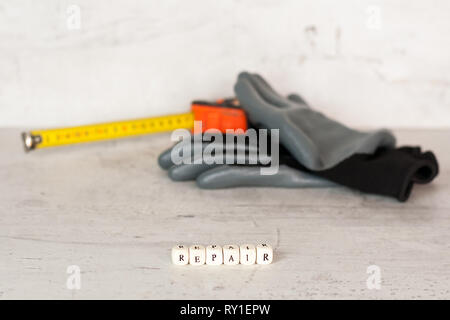 Costruzione nero guanti e un edificio tape sullo sfondo di un muro di cemento. In primo piano l'iscrizione riparazione. Foto Stock