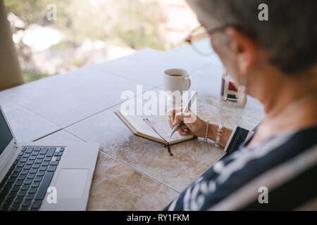 Close up donna senior iscritto in notebook a casa. Felice moderno lady in pensione con laptop seduto fuori sul balcone Foto Stock