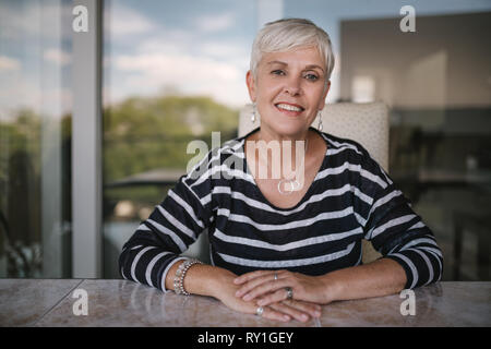 Bella donna anziana sorridente guardando nella telecamera. Ritratto di una donna matura con mani incrociate sul tavolo, fuori sul balcone. Bella Foto Stock