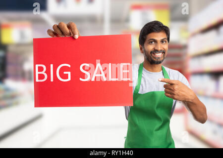 Indiano maschio supermercato o ipermercato dipendente azienda grande vendita testo su carta rossa con espressione gentile Foto Stock