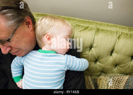 Angolo di Alta Vista del nonno che trasportano carino nipote dorme sulla spalla a casa Foto Stock