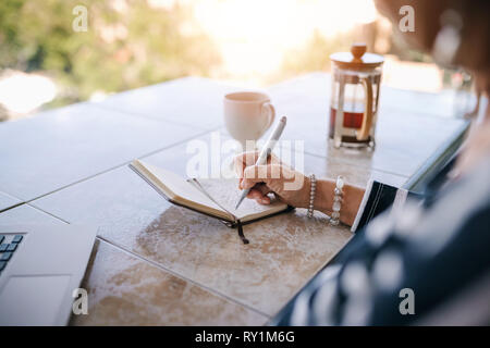 In prossimità di una donna matura la scrittura nel suo notebook mentre seduto fuori sul balcone con il sole di mattina attraverso la trasmissione via IR. Con sun flare Foto Stock