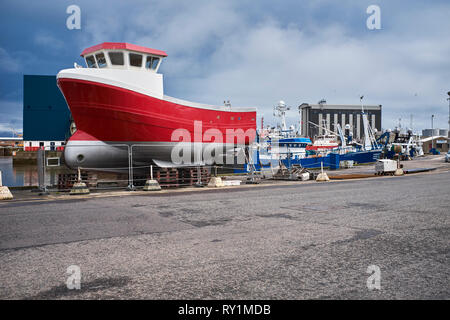 PETERHEAD, Aberdeenshire, Scotland, Regno Unito. Il 7 luglio 2017. Tra un trafficato porto lato una barca da pesca appoggia su procedure Dockside fuori dall'acqua per le riparazioni Foto Stock