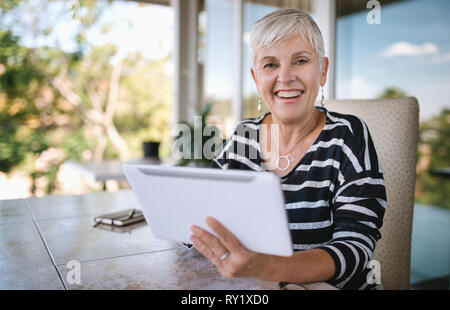 Ritratto di una donna matura sorridente, utilizzando il suo tablet a casa , al di fuori sul balcone. Bella donna anziana sorridente guardando nella telecamera Foto Stock