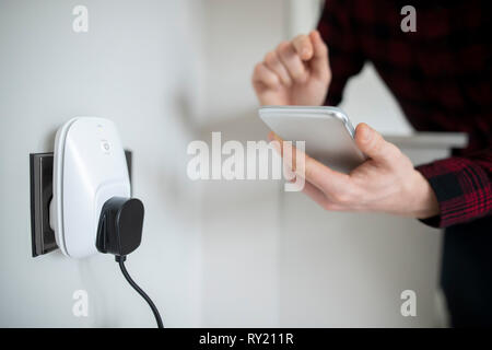 L'uomo il controllo Smart Plug utilizzando App sul telefono cellulare Foto Stock