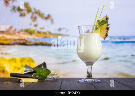 Il freddo La pina colada cocktail in un bicchiere sulla spiaggia con seascape sfondo Foto Stock