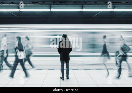 Una lunga esposizione foto con lonely giovane uomo colpo da dietro alla stazione della metropolitana con sfocata movimento del treno e a piedi le persone in background Foto Stock