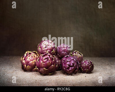 Carciofi crudi, Mediterraneo, vegetali non cotti su rustiche hessian, still life, luce pittura con texture. Foto Stock