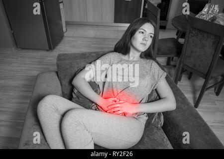 Giovane donna ha un stomachache, vista dall'alto, foto in bianco e nero, Accento colore rosso Foto Stock