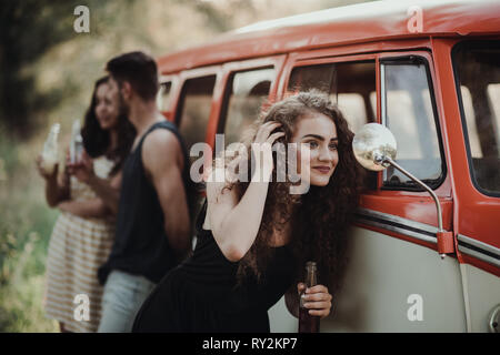 Un gruppo di giovani amici con bevande all'aperto permanente su un roadtrip attraverso la campagna, tenendo bottiglie. Foto Stock