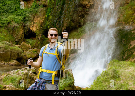 Bel giovane escursionista fermato accanto a una cascata di montagna di prendere un periodo di riposo Foto Stock