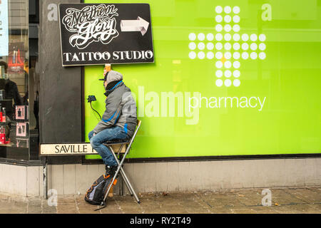 Uomo con un annuncio mobile per un tattoo shop di Newcastle, in Inghilterra, Regno Unito. Foto Stock