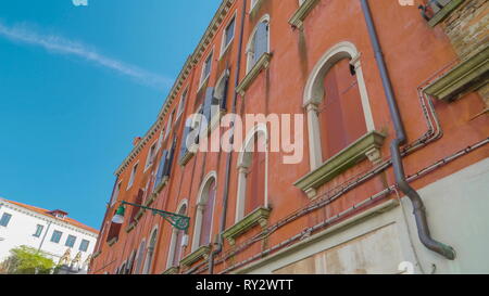 L'edificio rosso e il piccolo ponte di collegamento tra le due grandi edifici sulla piccola laguna di Venezia Italia Foto Stock