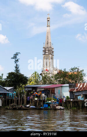 Xx secolo cattedrale cattolica Chiesa dietro tipico stagno vietnamita shack palafitte sul lungofiume del Co Chien fiume nel Delta del Mekong. In Cai Be Vietnam Foto Stock