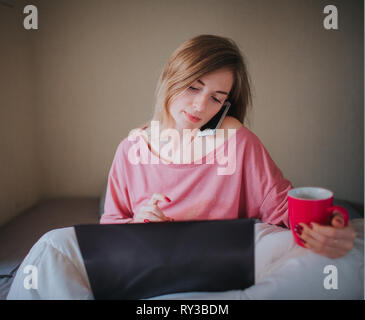 Una donna che lavora a casa e beve caffè. Il concetto di freelancing e multitasking Foto Stock