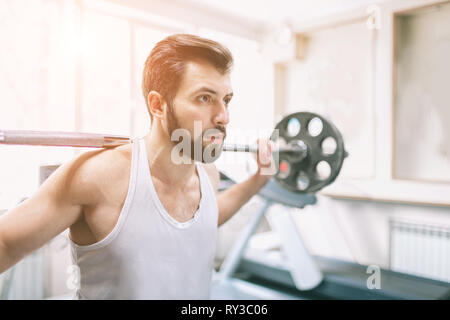 Muscolare uomo barbuto durante gli allenamenti in palestra. Allestitore fare sollevamento pesi . Chiusura del giovane femmina atletico model trains presso il fitness Foto Stock