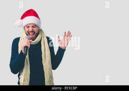 Ragazzo in un cappello di Natale il rock. Immagine di un uomo bello Cantare al microfono, isolato sulla luce. Ritratto emozionale di un ragazzo attraente su un Foto Stock