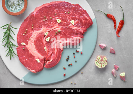 Bistecca di greggio. Carne con spezie e erbe aromatiche. Vista dall'alto sulla pietra di luce sullo sfondo. Foto Stock