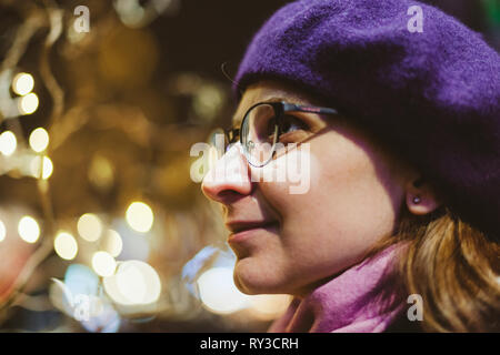 Ritratto di bella donna francese indossando trendy moda beret hat con defocalizzata bokeh luci del Mercatino di Natale in background Foto Stock