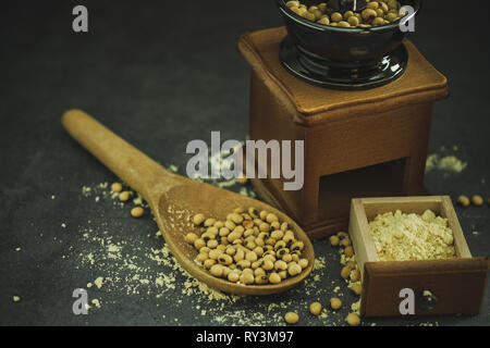 Macinino da caffè macinazione di semi di soia in polvere e il mestolo di legno nelle tenebre. Usato per fare il latte di soia. Foto Stock