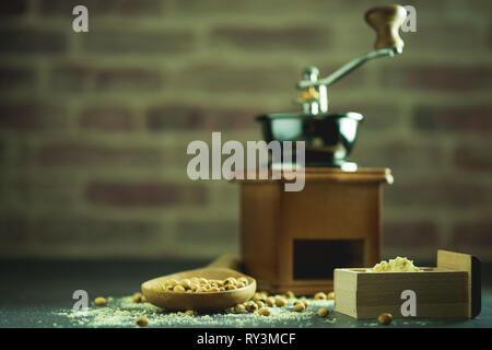 Macinino da caffè macinazione di semi di soia in polvere e il mestolo di legno nelle tenebre. Usato per fare il latte di soia. Foto Stock