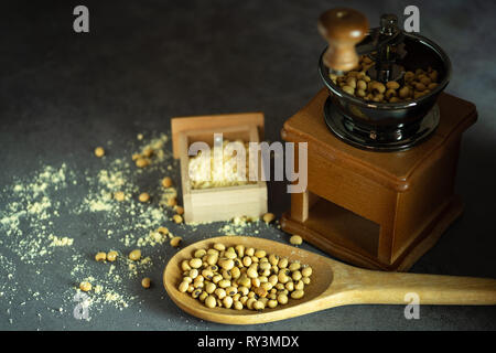 Macinino da caffè macinazione di semi di soia in polvere e il mestolo di legno nelle tenebre. Usato per fare il latte di soia. Foto Stock