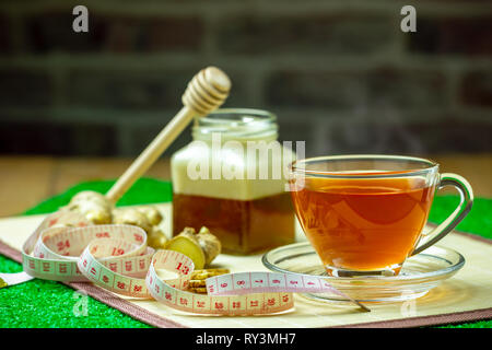 Succo di zenzero in una coppa trasparente e miele vaso collocato accanto con nastro di misurazione. Concetto di sano. Foto Stock