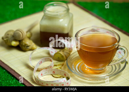 Succo di zenzero in una coppa trasparente e miele vaso collocato accanto con nastro di misurazione. Concetto di sano. Foto Stock