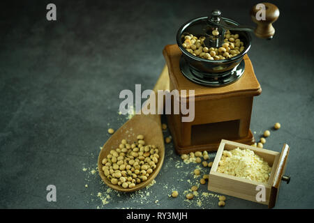 Macinino da caffè macinazione di semi di soia in polvere e il mestolo di legno nelle tenebre. Usato per fare il latte di soia. Foto Stock