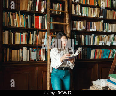 Bruna studentessa con libro in mani in un bookspace Foto Stock