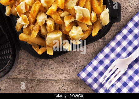 Poutine in un contenitore di asporto. Cucinato con patate fritte, carne di manzo con sugo di carne e formaggio. Cucina canadese. Foto Stock