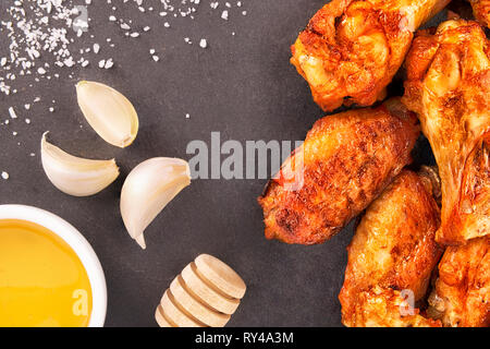 Ali di pollo con miele e aglio su un nero ardesia in background. Foto Stock