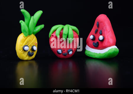 Plastilina figurine al buio su un tavolo di legno. Imitazione di ananas, angurie e fragole. Sfondo scuro. Foto Stock