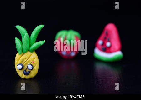 Plastilina figurine al buio su un tavolo di legno. Imitazione di ananas, angurie e fragole. Sfondo scuro. Foto Stock