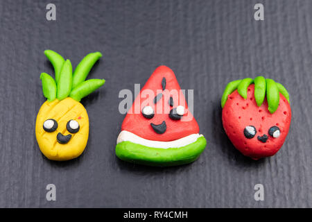 Plastilina figurine al buio su un tavolo di legno. Imitazione di ananas, angurie e fragole. Sfondo scuro. Foto Stock