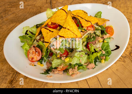 Insalata di tonno, lattuga iceberg, rucola, tortilla chips, mais, pomodori ciliegini e condimento balsamico. Foto Stock