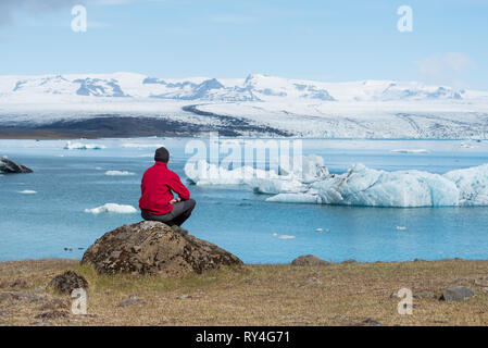 L'uomo traveler in giacca rossa si trova sulle sponde di un lago. Paesaggio estivo con laguna glaciale, di ghiacciai, iceberg nel sud-est dell' Islanda, Europa Foto Stock