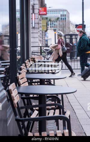 Londra, Regno Unito - Marzo 2019: Sedia vuota e tavoli sul marciapiede fuori Starbucks nella stazione Victoria di Londra Foto Stock