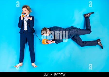Uomo numero di composizione mentre donna parlando al telefono su sfondo blu Foto Stock