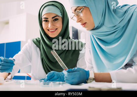 Femmina scienziati musulmani tenendo la pipetta e la provetta di vetro durante l'esperimento in laboratorio chimico Foto Stock
